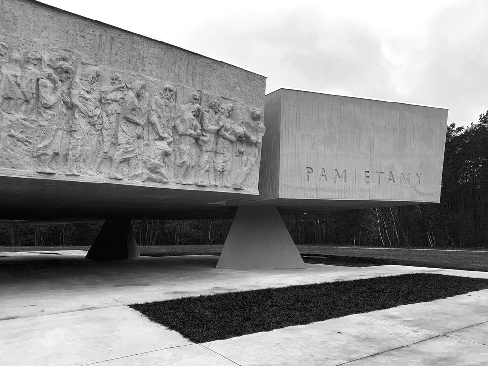 kamienny pomnik ofiar obozu zagłady w Chełmnie, dwie wielkoformatowe bryły o kształcie zbliżonym do prostopadłościanu, na lewej części płaskorzeźba przedstawiająca ludzkie postaci, na prawej słowo "pamiętamy"  (fot. E. Selman)