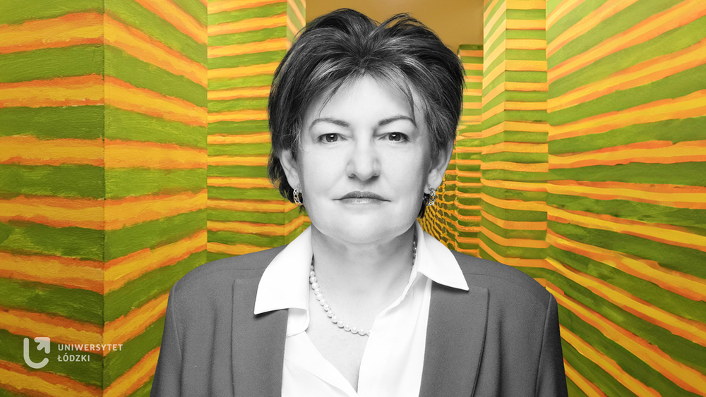 Prof. Aneta Pawłowska on the background of a painting installation by Leon Tarasewicz. This work consists of two parallel rows of 24 identical columns. They are located in a narrow, straight corridor that connects two different parts of the exhibition. The columns are painted with horizontal green, yellow and orange stripes.