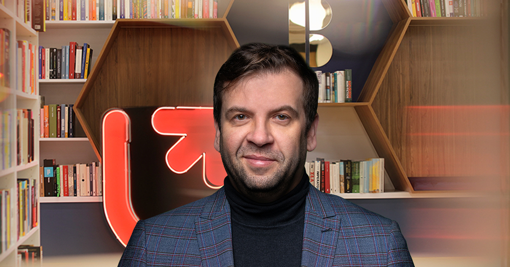 Prof. Chomczyński on the background of library shelves and a neon sign with the logo of the University of Lodz
