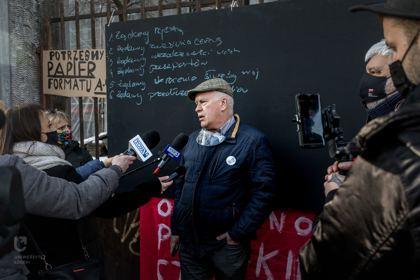 mężczyzna na tle transparentów udziela wywiadu dziennikarzom