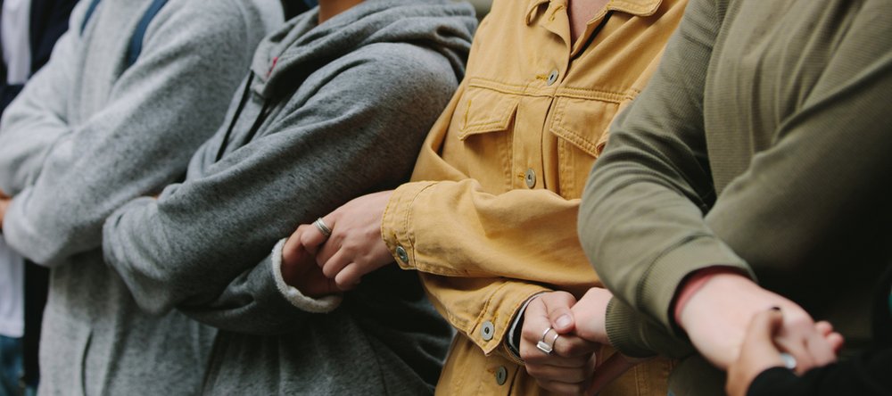 Sylwetki 4 osób stojących obok siebie i trzymających się za skrzyżowane ręce