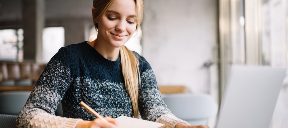 Na zdjęciu dziewczyna sporządza notatki przed komputerem